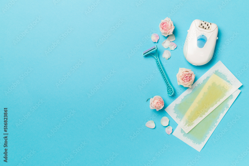Wax strips, modern epilator and razor with flowers on color background, top view Wax strips, modern epilator and razor with flowers on color background, top view