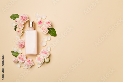 Cosmetic bottle with rose flower on color background, top view