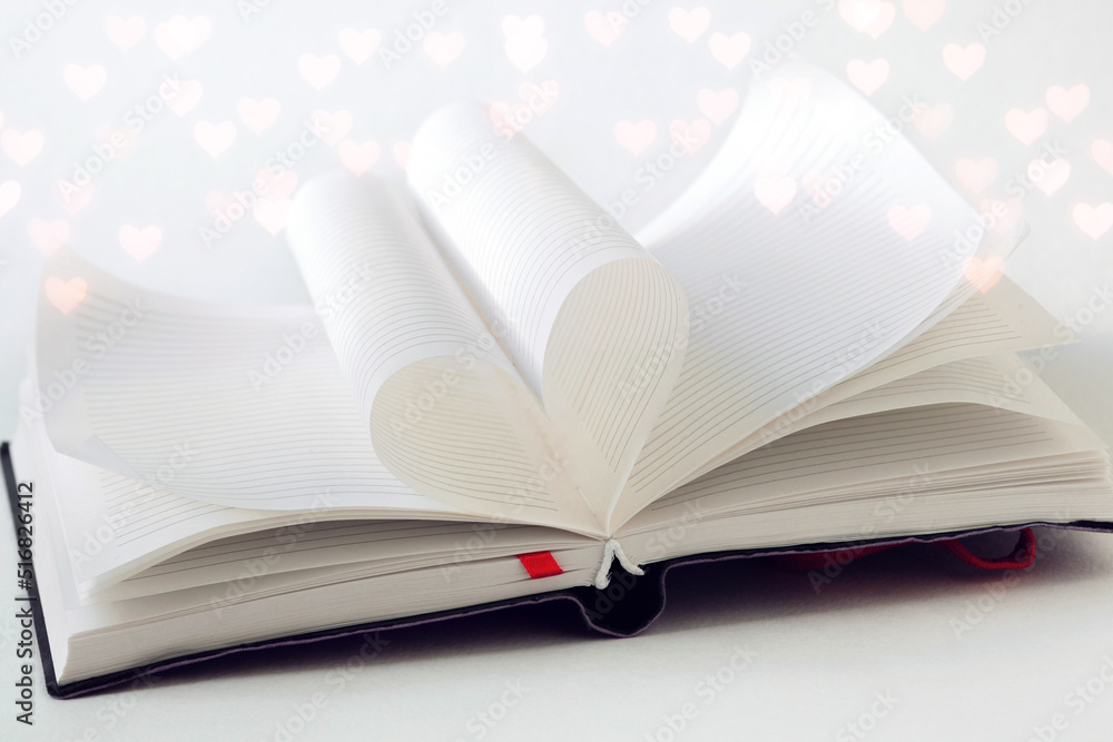 Open book, two pages in the book are folded in the shape of a love heart, bokeh hearts around, love to read books, valentines day background Open book, two pages in the book are folded in the shape of a love heart, bokeh hearts around, love to read books, valentines day background