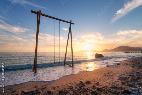 Fototapeta Naklejka Na Ścianę i Meble -  Wooden swing in beautiful blue sea with waves, sandy beach, sky with golden sunlight at sunset in summer. Vacation in Oludeniz, Turkey. Tropical landscape with swing on sea coast, water. Travel