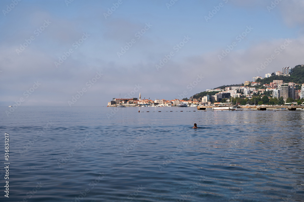 Woman swims in the sea against the background of buildings on the coast