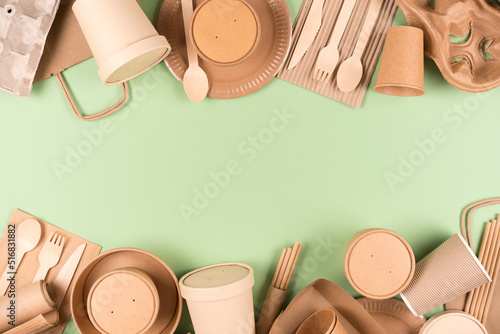 Frame made with eco paper utensils and wooden bamboo cutlery set, food containers and paper cups over light green background with copy space. Sustainable food packaging concept
