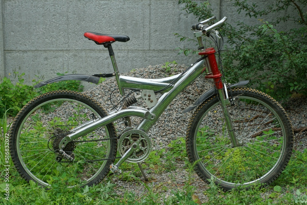 old iron heavy chrome sports mountain bike stands on the street in green grass in summe