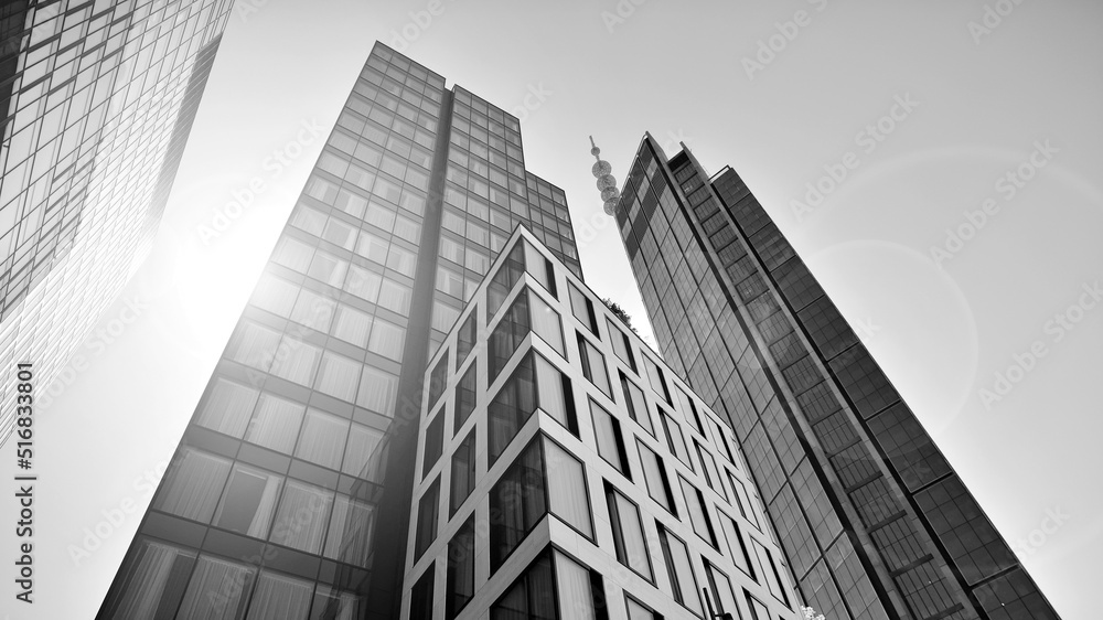 Fototapeta premium Bottom view of modern skyscraper in business district against blue sky. Looking up at business buildings in downtown. Rising sun on the horizon. Black and white.