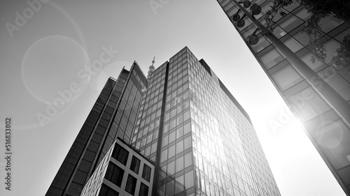 Bottom view of modern skyscraper in business district against blue sky. Looking up at business buildings in downtown. Rising sun on the horizon. Black and white.