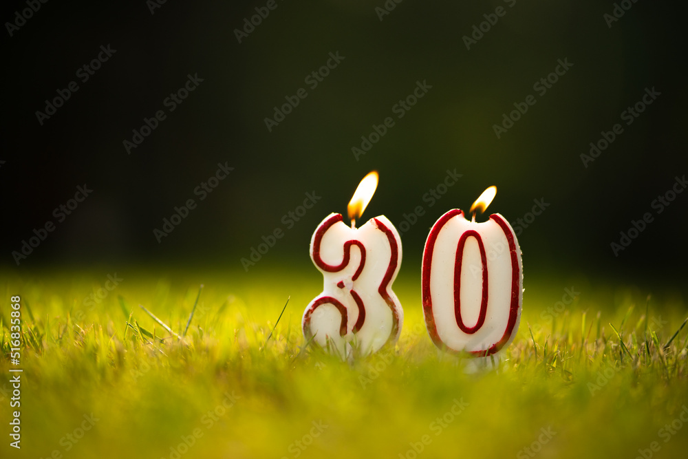 Candles in the form of the number 30 on a green summer background. Thirtieth anniversary. Congratulations on the anniversary of thirty years. - obrazy, fototapety, plakaty 