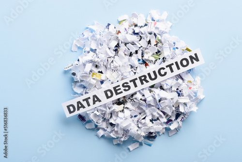 Words Data destruction on top of heap of cross cut shredded paper on blue background top view