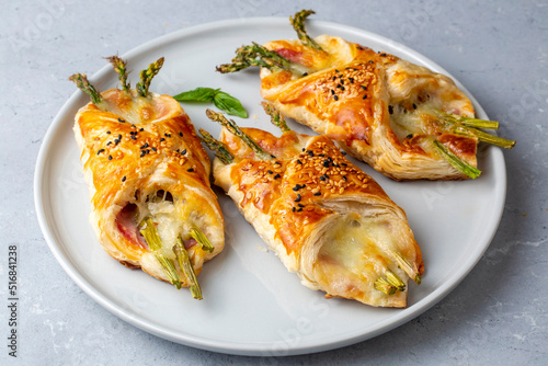 Baked green asparagus with ham and cheese in puff pastry sprinkled with sesame seeds and green basil leaves.
