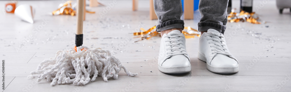 Young man with mop cleaning messy room after party, closeup of legs. Banner design