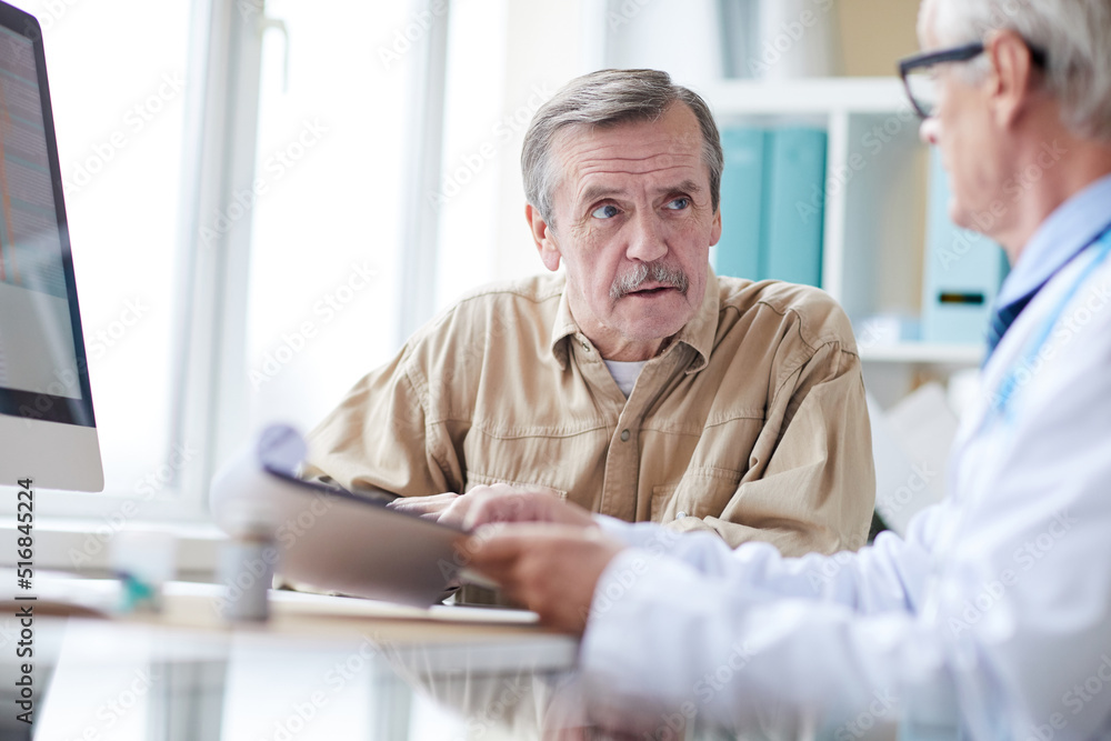 Pensive aged man with mustache sitting at table and talking to doctor at medical consultation Pensive aged man with mustache sitting at table and talking to doctor at medical consultation