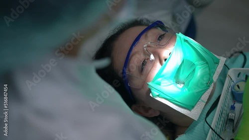 High angle view portrait of Caucasian woman in rubber dam on dental chair with doctor inserting root canal file in dental canal. Unrecognizable dentist doing procedure for patient in hospital indoors photo