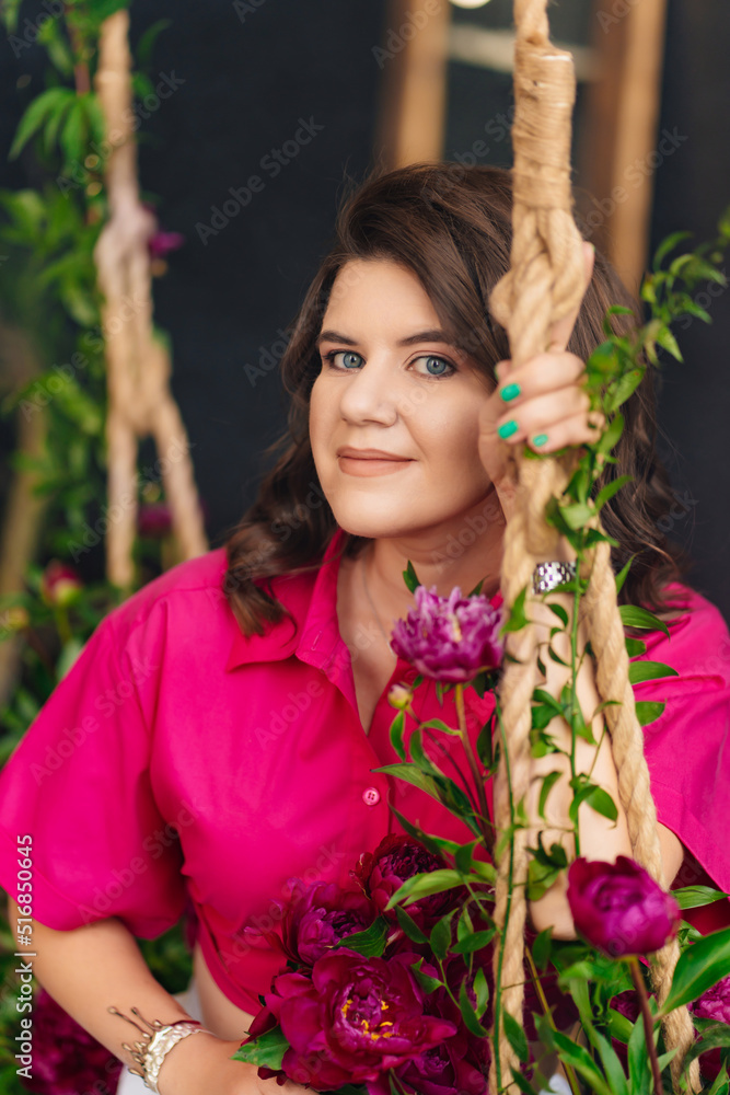 a brunette woman in a pink blouse with peonies on the swing. a brunette woman in a pink blouse with peonies on the swing.