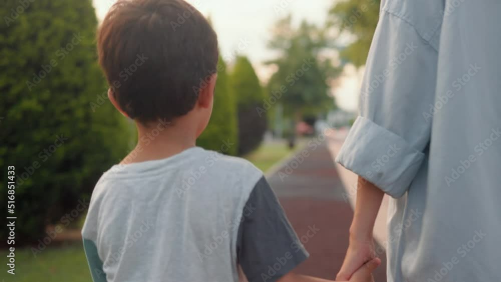 Back view of preschooler holding mom's hand and walking along the alley Back view of preschooler holding mom's hand and walking along the alley