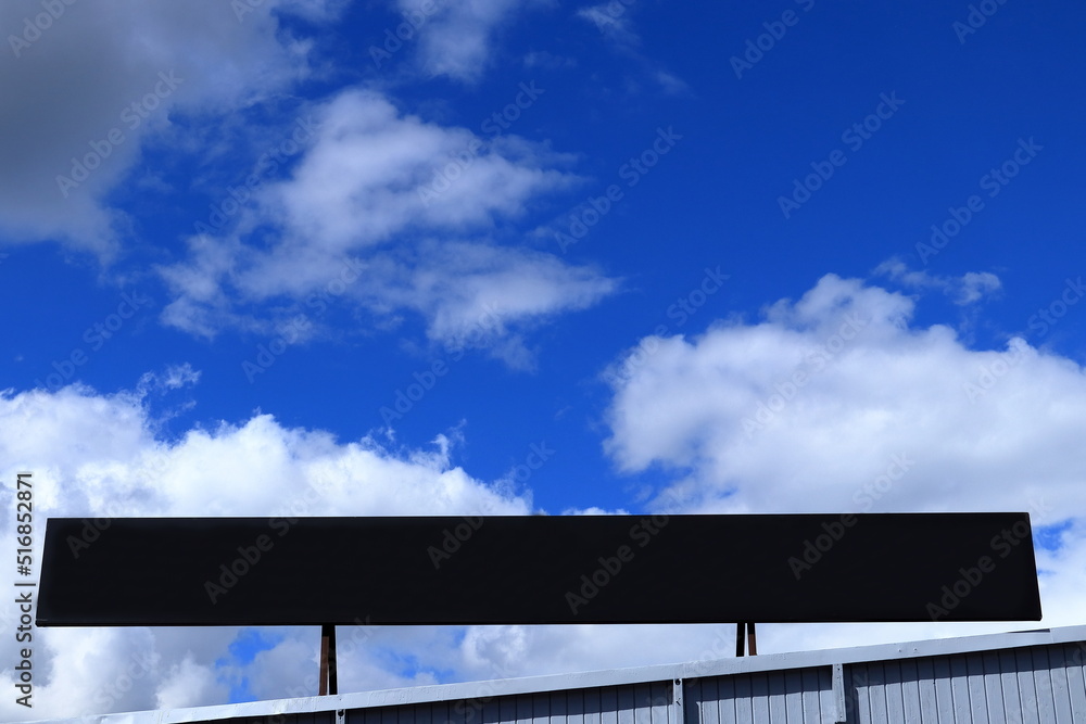 One empty black or gray sign. Ready for your design. Copy space. Clouds and sky in the background. Sunny day outside.