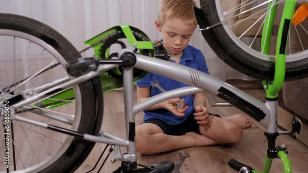 A little boy is repairing a bike at home on the floor, the bike is upside down. A child holds a wrench before starting a bicycle repair. A little boy is repairing a bike at home on the floor, the bike is upside down. A child holds a wrench before starting a bicycle repair.