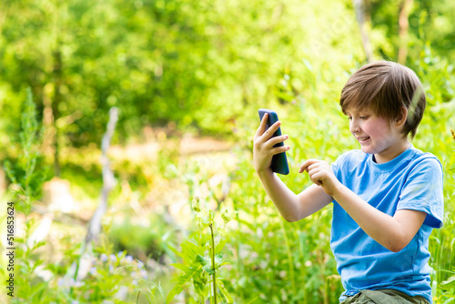 little boy is resting in nature, sitting on a log and chatting through a mobile phone in social networks