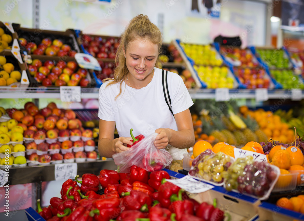 Fifteen-year-old girl who came to the supermarket chooses a red bell pepper, putting it in a package to buy it