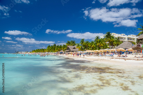 Fototapeta Naklejka Na Ścianę i Meble -  People swimming near white sand beach with umbrellas, bungalow bar and cocos palms, turquoise caribbean sea, Isla Mujeres island, Caribbean Sea, Cancun, Yucatan, Mexico