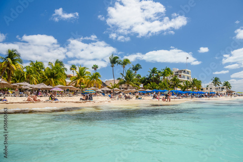 Fototapeta Naklejka Na Ścianę i Meble -  People sunbathing on the white sand beach with umbrellas, bungalow bar and cocos palms, turquoise caribbean sea, Isla Mujeres island, Caribbean Sea, Cancun, Yucatan, Mexico