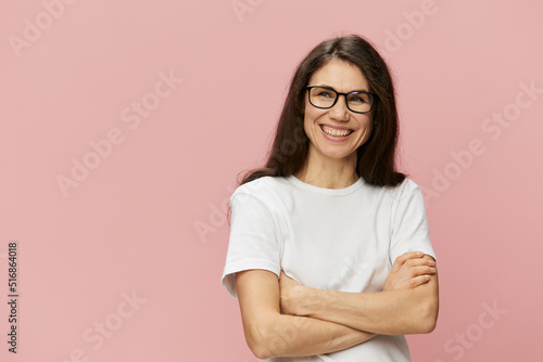 portrait of a cute, attractive brunette in a white tank top on a pink background, with a pleasant smile, standing in glasses for vision