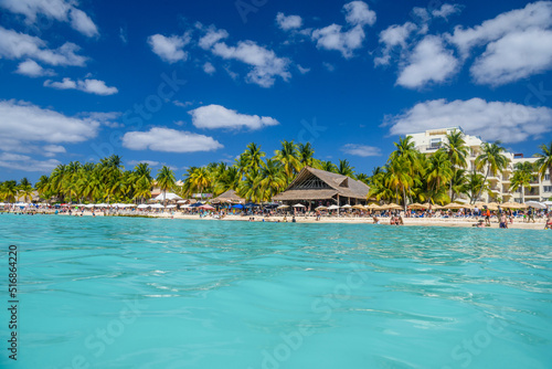 People swimming near white sand beach with umbrellas, bungalow bar and cocos palms, turquoise caribbean sea, Isla Mujeres island, Caribbean Sea, Cancun, Yucatan, Mexico