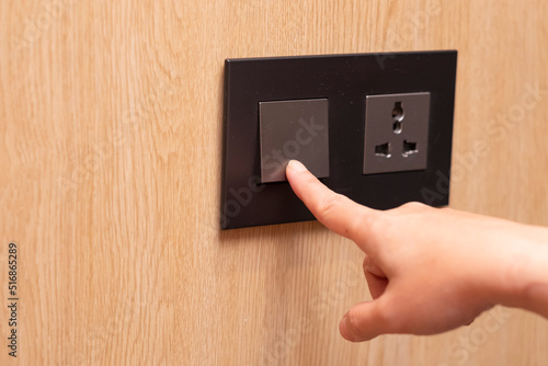 Light-switches and electrical plug connector at wooden wall. A finger is about to turn light off.