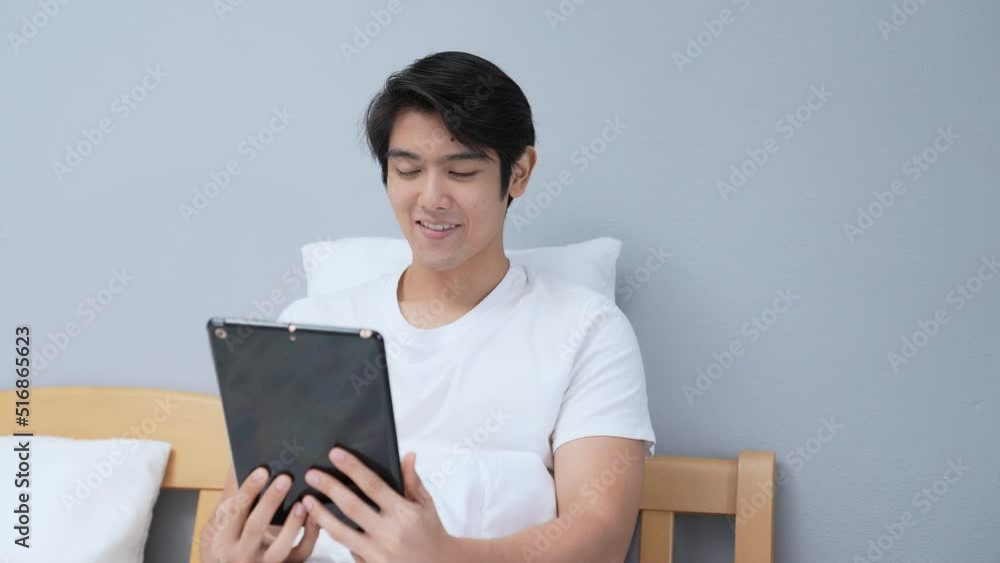 Holiday concept of 4k Resolution. Asian man playing tablet in bedroom. Holiday concept of 4k Resolution. Asian man playing tablet in bedroom.