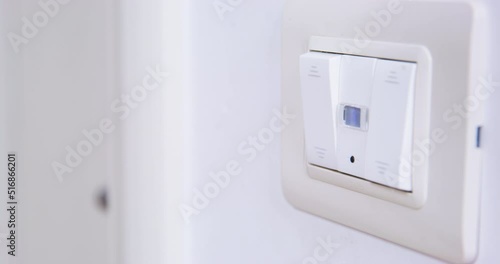 Hand of man presses switch on white wall to turn off light in corridor of apartment. Owner goes out to another room closing door closeup photo