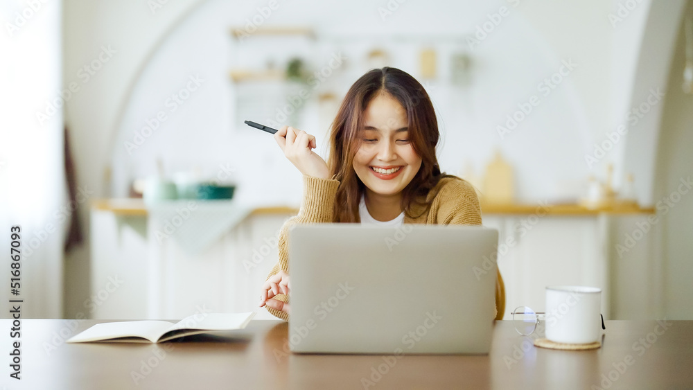 Young asian woman sitting at table and taking notes in notebook. Working on table with computer laptop, document paperwork and cup of coffee. Student learning online Young asian woman sitting at table and taking notes in notebook. Working on table with computer laptop, document paperwork and cup of coffee. Student learning online