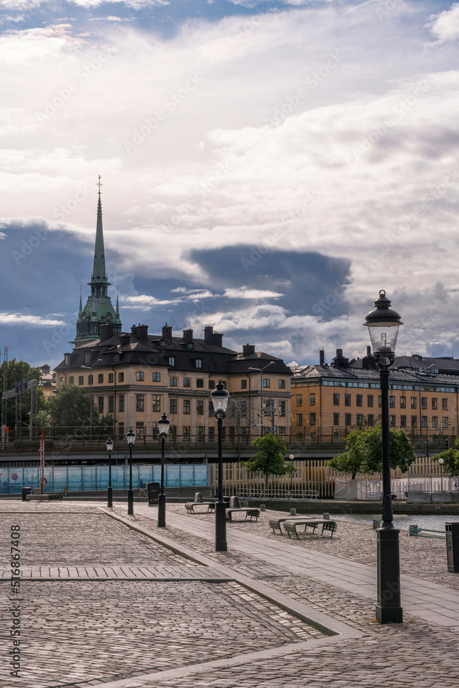 Dark skies over the German church and apartment buildings in the old town Gamla Stan and a pier with lamp pools, a summer day in Stockholm
