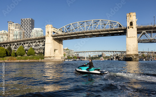 Adventurous Caucasian Woman on Water Scooter riding in the Ocean. Sunny Sunset Sky. Downtown Vancouver, British Columbia, Canada. Burrard Bridge. photo