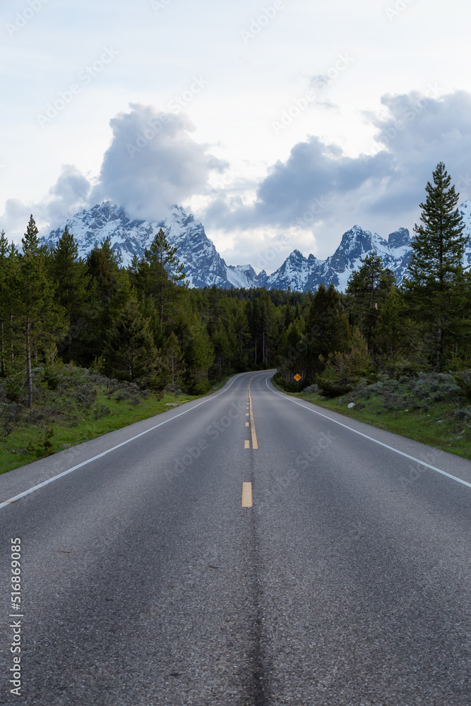 Scenic Road surrounded by Mountains and Trees in American Landscape. Spring Season. Grand Teton National Park. Wyoming, United States. Nature Background. Scenic Road surrounded by Mountains and Trees in American Landscape. Spring Season. Grand Teton National Park. Wyoming, United States. Nature Background.