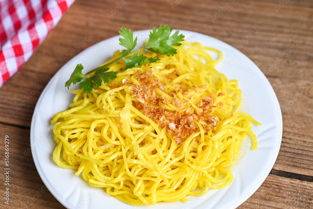 yellow noodles on white plate and wooden background , instant noodles yellow noodles rice vermicelli food with fried garlic and coriander yellow noodles on white plate and wooden background , instant noodles yellow noodles rice vermicelli food with fried garlic and coriander