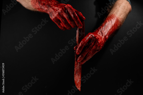 Man holding knife with bloody hand on black background.  photo