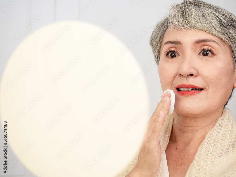 Portrait of mature aged asian woman 50s touching face skin looking in mirror reflection. healthy moisturized skin care, aging beauty, skincare treatment cosmetics concept. Portrait of mature aged asian woman 50s touching face skin looking in mirror reflection. healthy moisturized skin care, aging beauty, skincare treatment cosmetics concept.