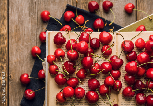 Atmospheric photo of ripe red sweet cherries and books on the rustic wooden background. Selective focus. Shallow depth of field.