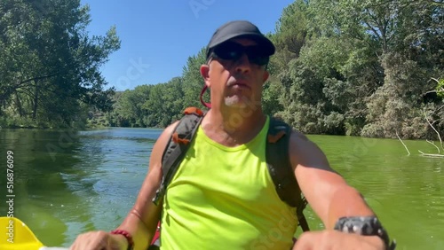 Middle aged kayaker wearing a yellow sleeveless shirt, a black cap, a backpack and sunglasses in a green water river in SE Spain. photo