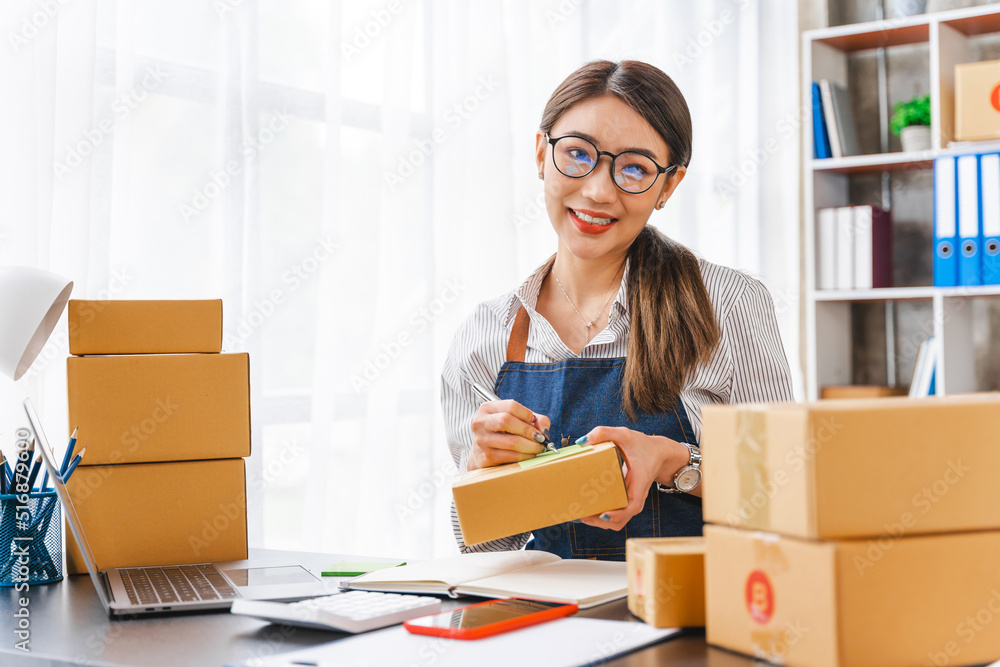 Looking Camera, Startup small business entrepreneur or freelance Asian woman using a laptop with box, online marketing packaging box and delivery, SME concept. Looking Camera, Startup small business entrepreneur or freelance Asian woman using a laptop with box, online marketing packaging box and delivery, SME concept.