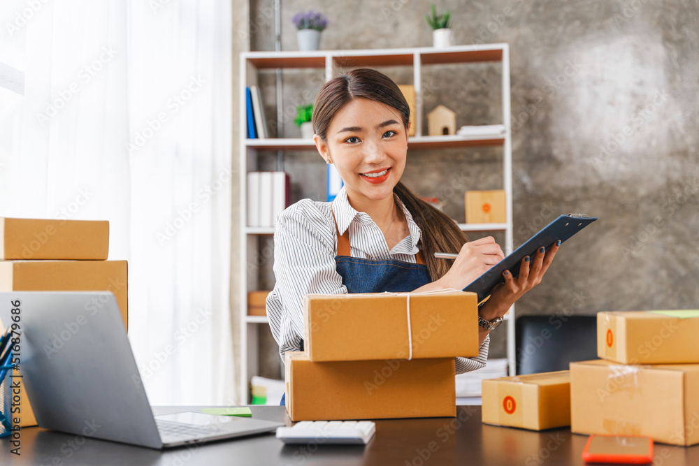 Looking camera, Start up successful small business owner, a freelance young Asian female merchant preparing a package box to deliver to customers, SME entrepreneurs. Looking camera, Start up successful small business owner, a freelance young Asian female merchant preparing a package box to deliver to customers, SME entrepreneurs.
