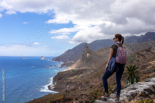 Backpack woman with scenic view of Atlantic Ocean coastline and Anaga mountain range on Tenerife, Canary Islands, Spain, Europe. Looking at Roque de las Animas crag. Hiking trail from Afur to Taganana