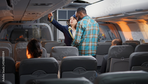 Group of diverse passengers boarding on airplane seats, talking to flight attendant on airline service. Flying and travelling with commercial airline, chatting with stewardess about service.