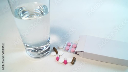 A glass of water, a number of multi-colored tablets and a box with a blister