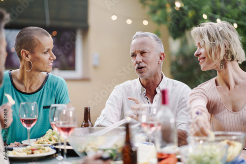Mature Man husband talking with female friend and wife during summer dinner at home