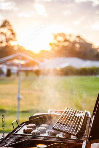 Rissoles cooking on a BBQ in the backyard at sunset photo