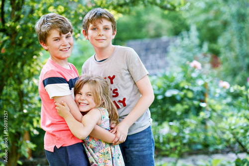 Portrait of three siblings children. Two kids brothers boys and little cute toddler sister girl having fun together in domestic garden. Happy healthy family playing, walking, active leisure on nature