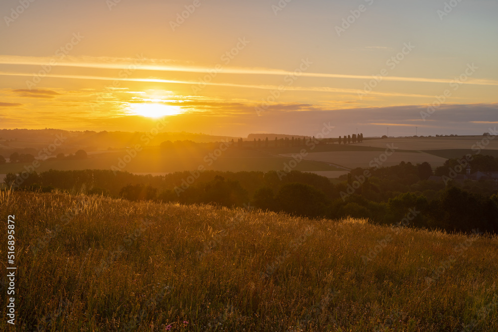Fototapeta premium Spectacular sunrise in the rolling hill landscape in the south of Limburg with a view on the meadows and on a row of poplar trees, creating the feeling of being in the Siena Province of Italy.