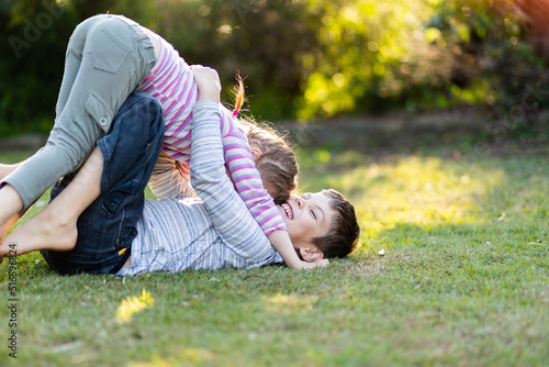 Brother and sister play fighting together on lawn in garden photo