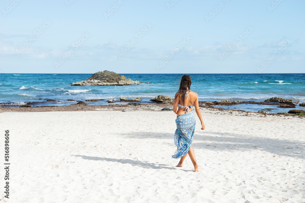 Young woman wearing bikini and sarong walking on beach Young woman wearing bikini and sarong walking on beach