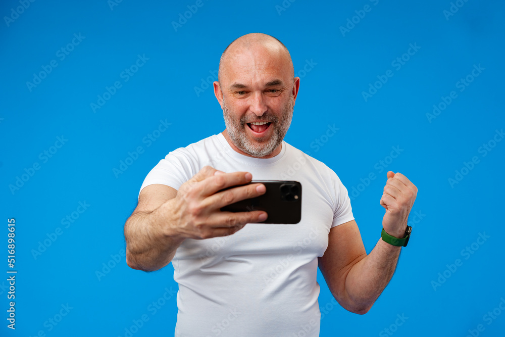 Happy middle-aged man with a phone in his hands against blue background Happy middle-aged man with a phone in his hands against blue background