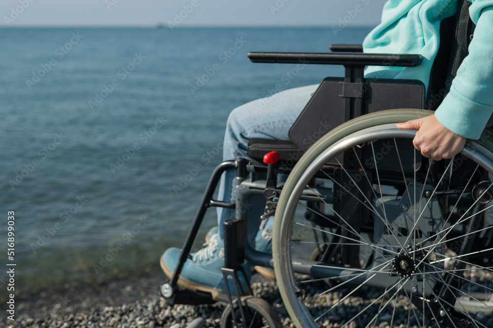 Naklejka premium Caucasian woman in a wheelchair on the seashore. Close-up of female hands.